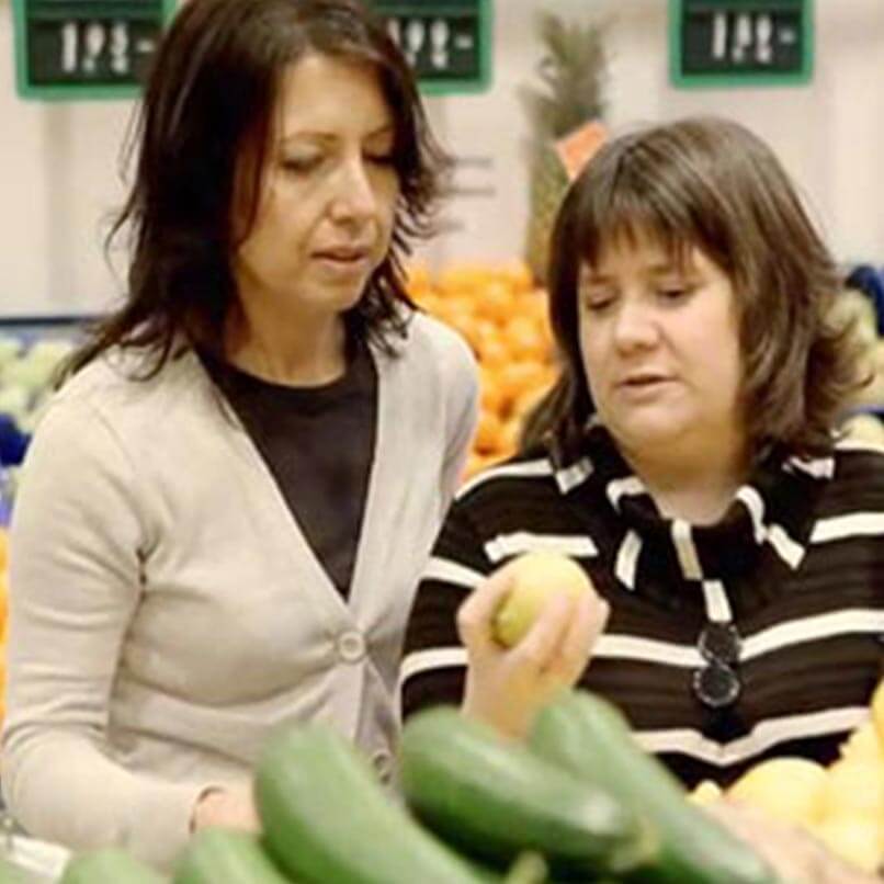 Una mujer con discapacidad visual explica a otra mujer cómo elige la fruta en el supermercado.