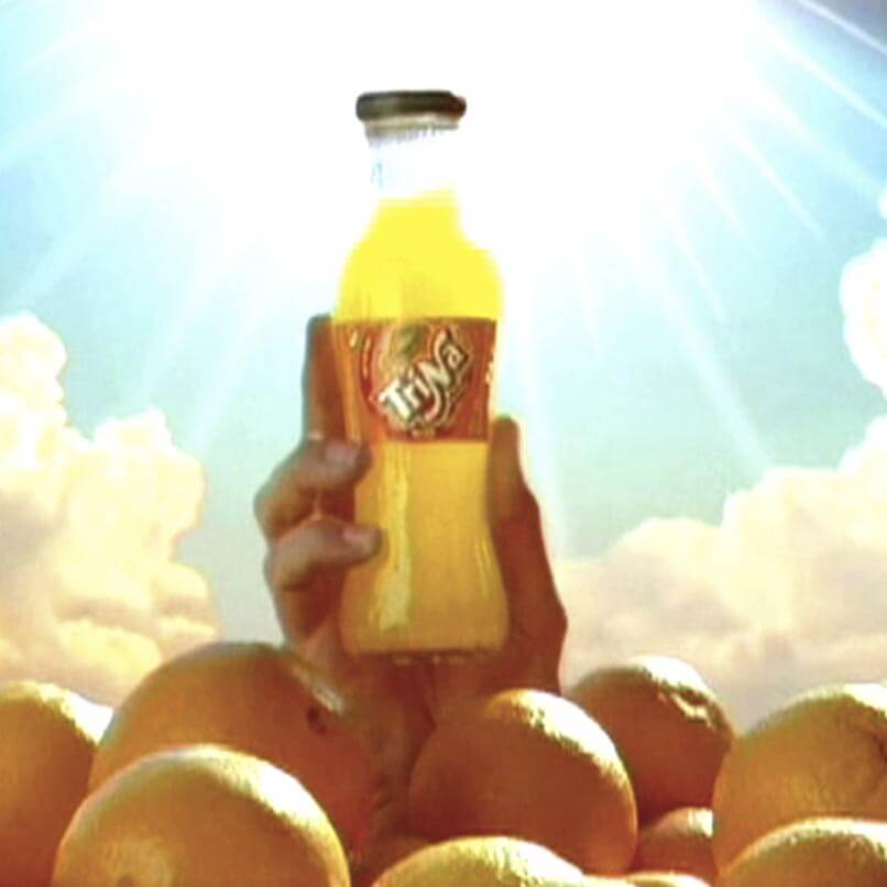 Una mano aparece de entre un montón de naranjas sosteniendo una botella de Trina